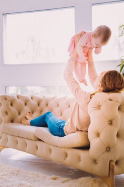 Kanepede oturan ve bebeği havada yukarı kaldırarak Genç Anne