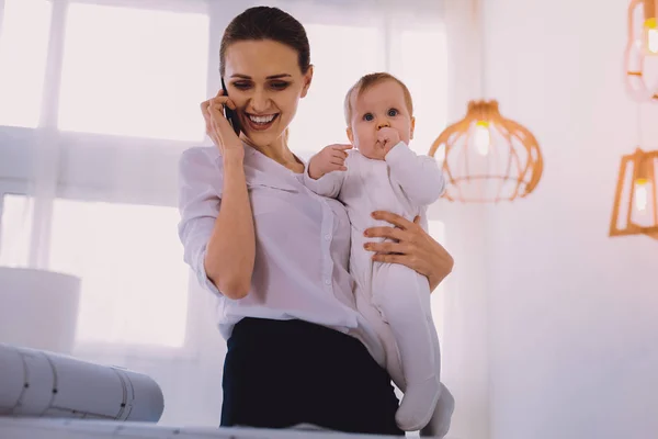 Ingeniero positivo hablando por teléfono mientras se queda en casa con el bebé —  Fotos de Stock