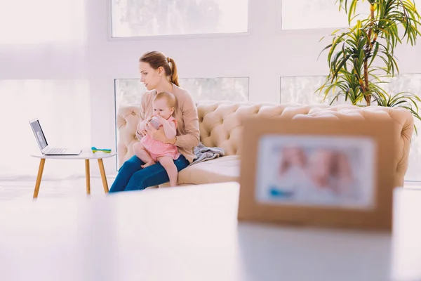 Young woman sitting with a baby and looking at the screen of her laptop — Stock Photo, Image