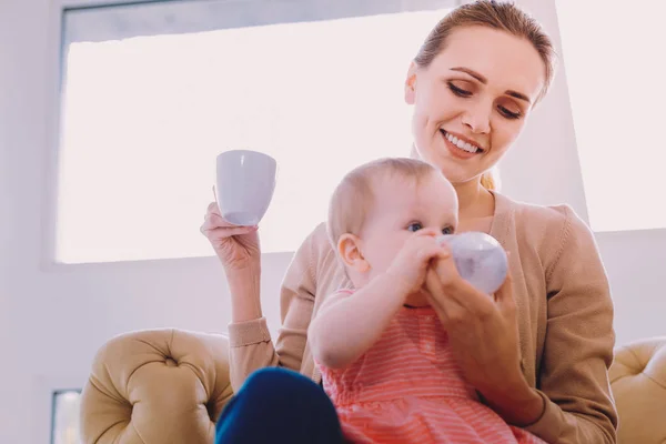 Caring mother smiling while giving a bottle of water to her adorable baby — Stock Photo, Image