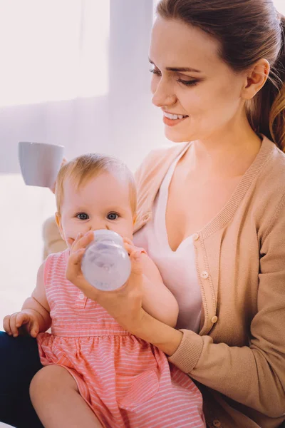 Mujer joven bebiendo té mientras su bebé bebe agua —  Fotos de Stock