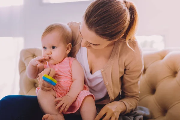 Young mother holding a rattle while sitting with a baby — Stock Photo, Image