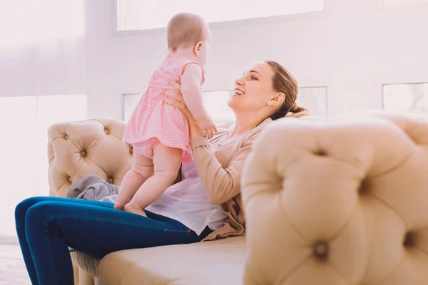 Kanepede rahatlatıcı ve bebeği ile oynayan genç anne — Stok fotoğraf