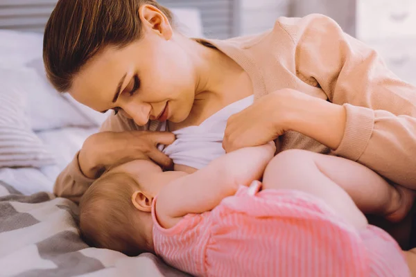 Hungriges Mädchen liegt neben ihrer stillenden Mutter — Stockfoto