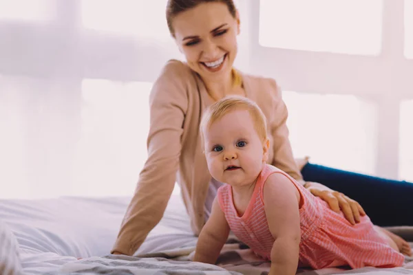 Schönes Baby sieht neugierig aus, während es in der Nähe ihrer lächelnden Mutter liegt — Stockfoto