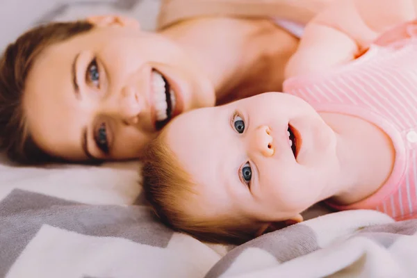 Mujer emocional sonriendo mientras se relaja en la cama con su bonito bebé —  Fotos de Stock