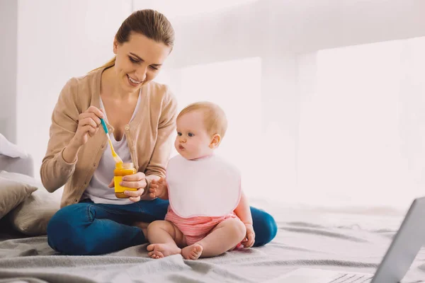 Cuidadosa niñera sosteniendo un frasco de comida para bebés mientras alimenta a un niño —  Fotos de Stock