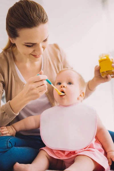 Accurata madre sorridente mentre alimenta sua figlia con cibo per bambini — Foto Stock