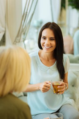 Keyifli zaman. Bir bardak çay ile oturan annesine dinlerken neşeli esmer kadın