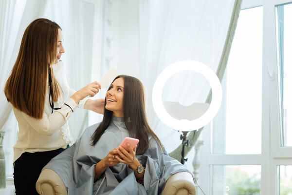 Positive joyful woman looking at her hair stylist
