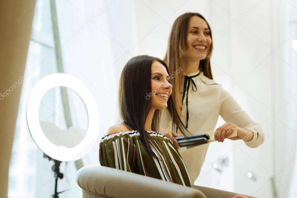 Positive nice woman using a hair straightener