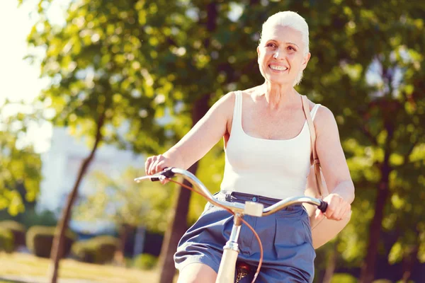 容光焕发的退休女子笑着宽, 而骑自行车 — 图库照片
