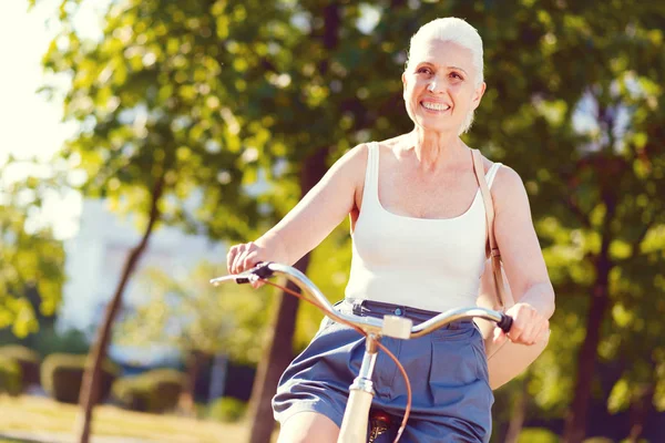 Stralende gepensioneerde vrouw breed grijnzend tijdens het fietsen — Stockfoto