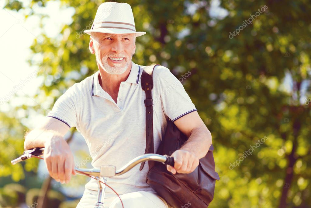 Stylish senior gentleman smiling while leaning on bicycle