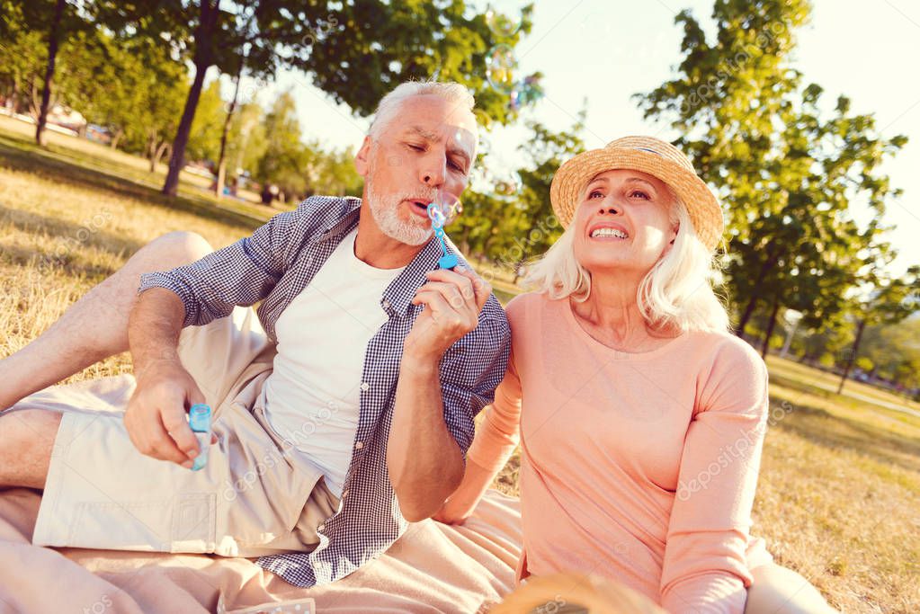 Nostalgic retired couple blowing soap bubbles in summer park