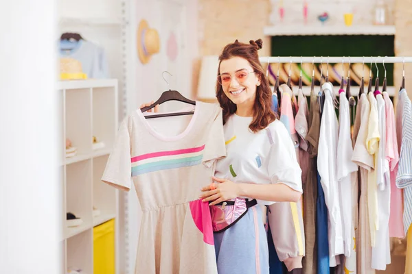 Beaming woman being fond of pink clothes buying new dress