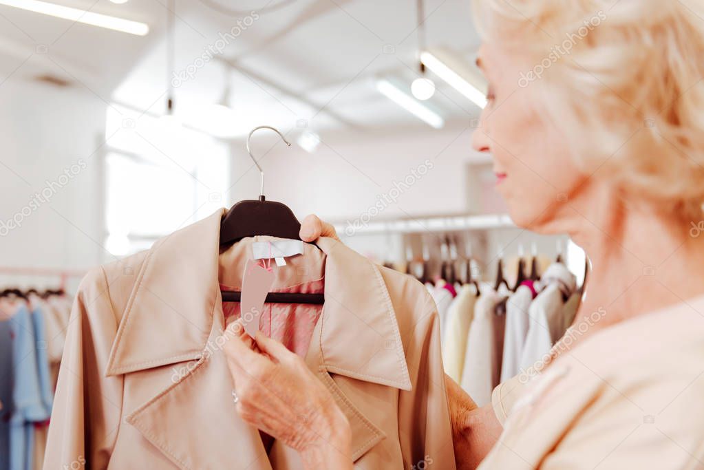 Stylish woman holding price tag of coat while shopping