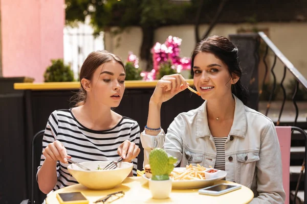 Dark-haired woman feeling jealous while watching her friend eating fries — Stock Photo, Image