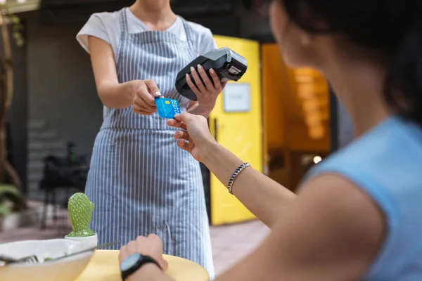 Mladá servírka nošení jednotné užívání debetní karty, její klienta — Stock fotografie
