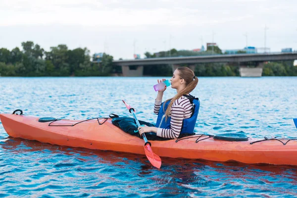 Blondhaarige Frau sitzt im Kanu und trinkt Wasser — Stockfoto