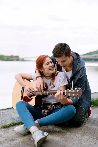 Creative hobby. Nice handsome man standing behind his girlfriend while helping her to play the guitar