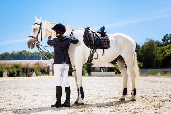 Appealing dark-haired woman standing near white saddle horse — Stock Photo, Image