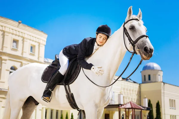 Businesswoman fond of equestrianism hugging her white horse