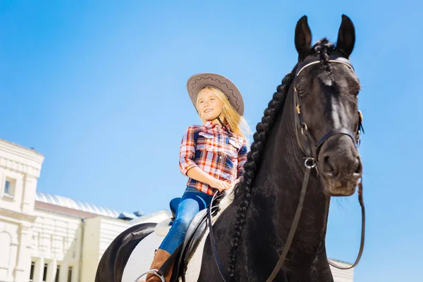 Mosolygó lány farmert visel és lovaglás csizma, ül a sötét ló — Stock Fotó