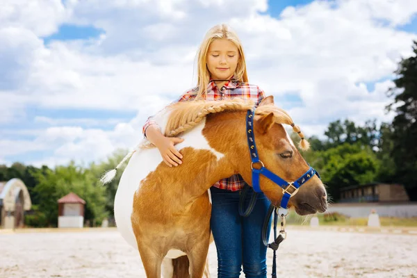Caring pleasant girl hugging little cute pony with braid — Stock Photo, Image