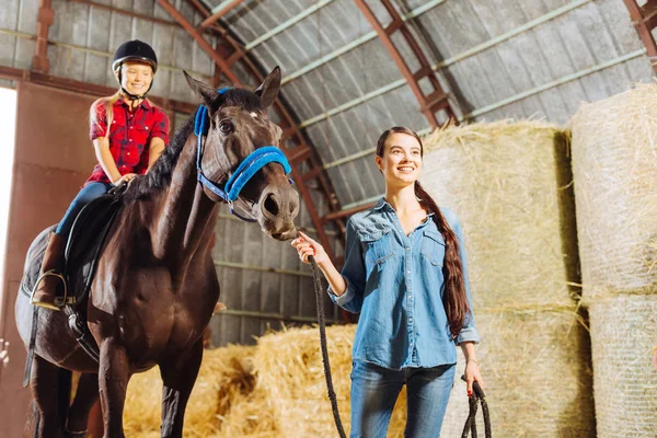 Dark-haired stylish riding teacher leading horse with cute girl