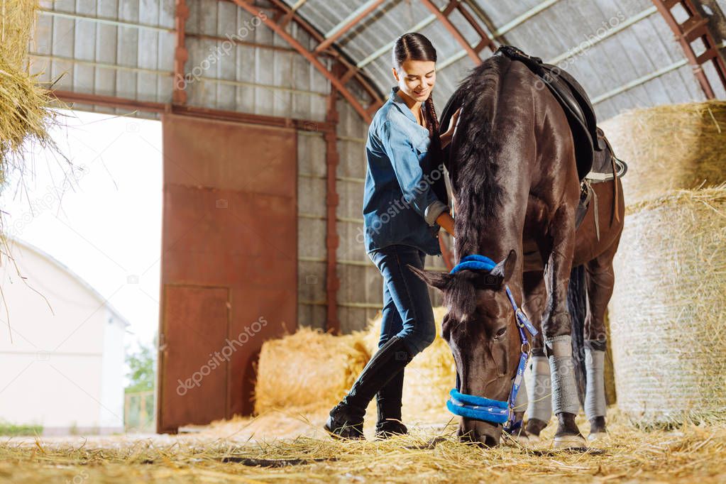 Professional female rider feeling good while visiting horse in stable