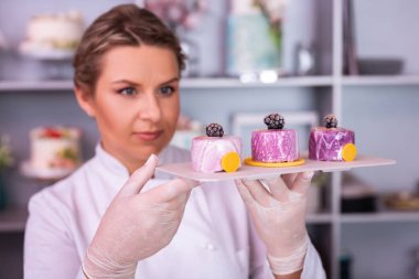 Kadın şef mavi gözlü beyaz plaka üç meyve kek ile tutarak
