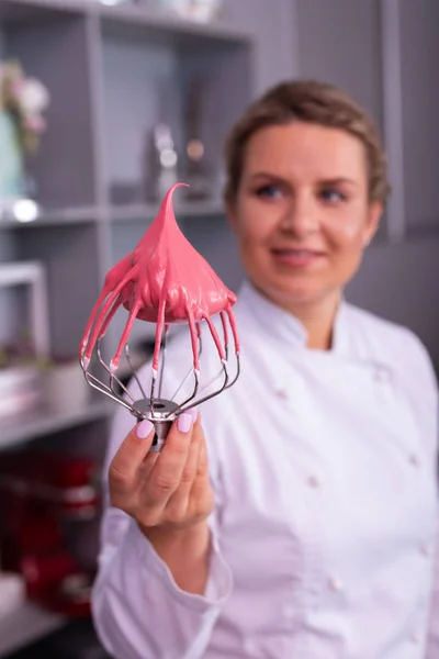 Berömda sockerbagare håller verktyget visp med rosa maräng — Stockfoto
