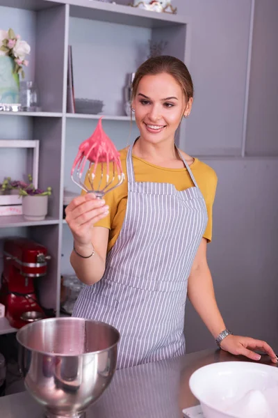 Smiling woman wearing striped apron holding utility whisk with meringue