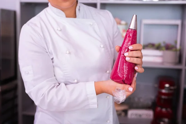 Chef mujer sosteniendo bolsa de pastelería con postre de cocina merengue rosa —  Fotos de Stock