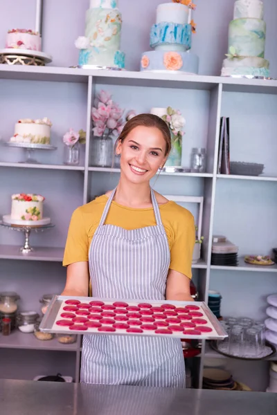 S úsměvem baker stojí pan plné světle růžové makronky — Stock fotografie