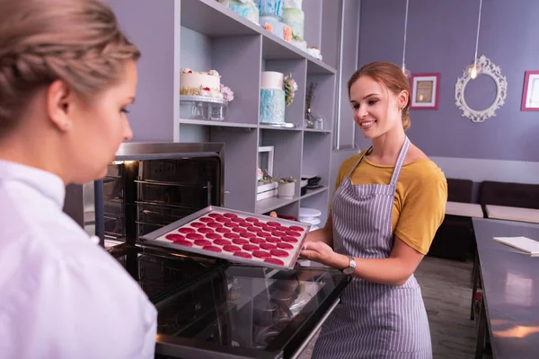 Assadeira promissora colocando assadeira com macaroons no forno — Fotografia de Stock