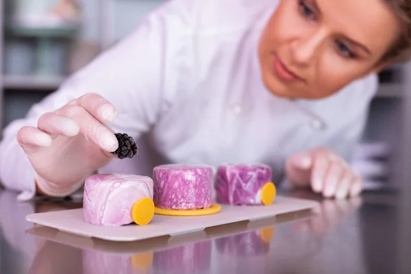 Baker versieren van taarten met spiegel suikerglazuur met sommige bessen — Stockfoto