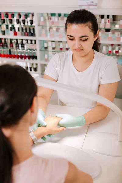 Jeune maître des ongles aux cheveux bruns fournissant un service à sa cliente — Photo