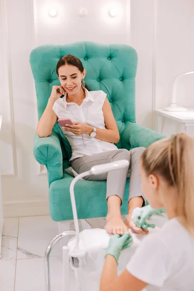 Mulher de negócios de cabelos escuros lendo seu e-mail enquanto pedicure — Fotografia de Stock