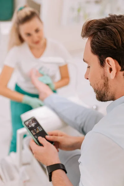 Homme aux cheveux foncés utilisant son téléphone intelligent tout en profitant de massage des pieds — Photo