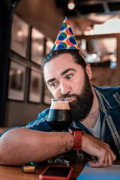 Смешной бородатый мужчина потягивает тёмное пиво в честь дня рождения. — стоковое фото