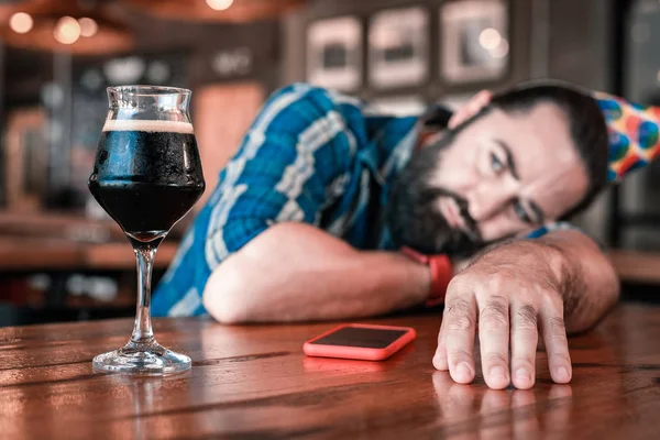 Hombre de pelo oscuro barbudo mirando un vaso de buena cerveza fría oscura — Foto de Stock
