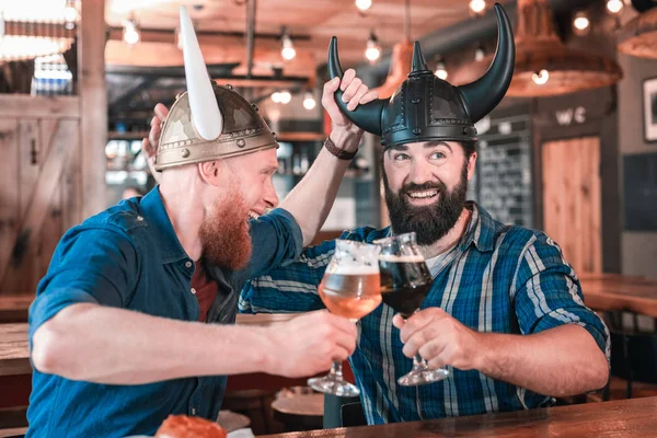 Due uomini maturi divertenti che indossano cappelli vichinghi seduti in pub tematico — Foto Stock