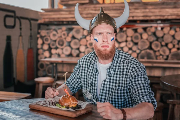 Capelli rossi uomo barbuto indossa cappello vichingo mangiare il suo hamburger — Foto Stock