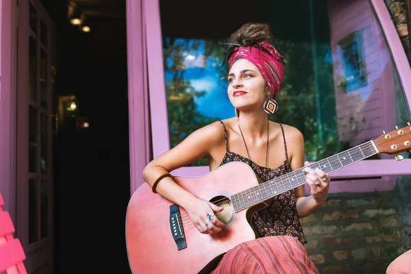 Donna che indossa orecchini luminosi suonare la chitarra al di fuori caffè — Foto Stock