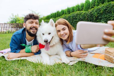 Blonde-haired woman making selfie with her husband and dog clipart