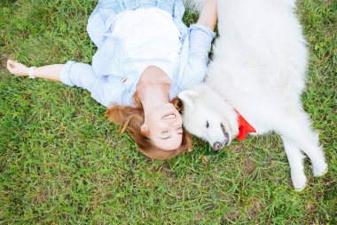 Smiling blonde-haired woman lying on grass with her white dog clipart