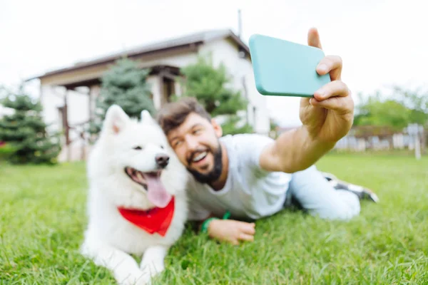 Lächelnder Mann hält sein blaues Smartphone in der Hand und macht Foto mit Husky — Stockfoto