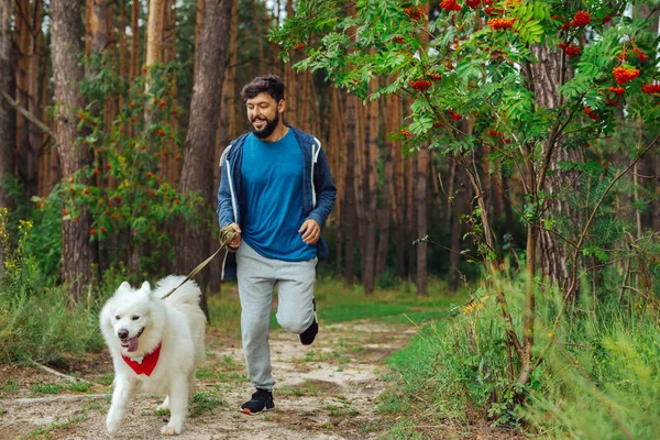 Bearded man wearing sport suit running with dog in the forest